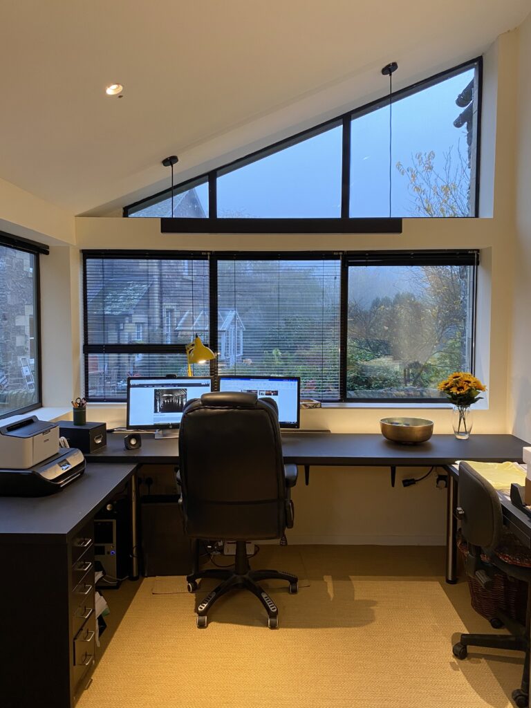A photo of a home office with desk and office chair in front of window