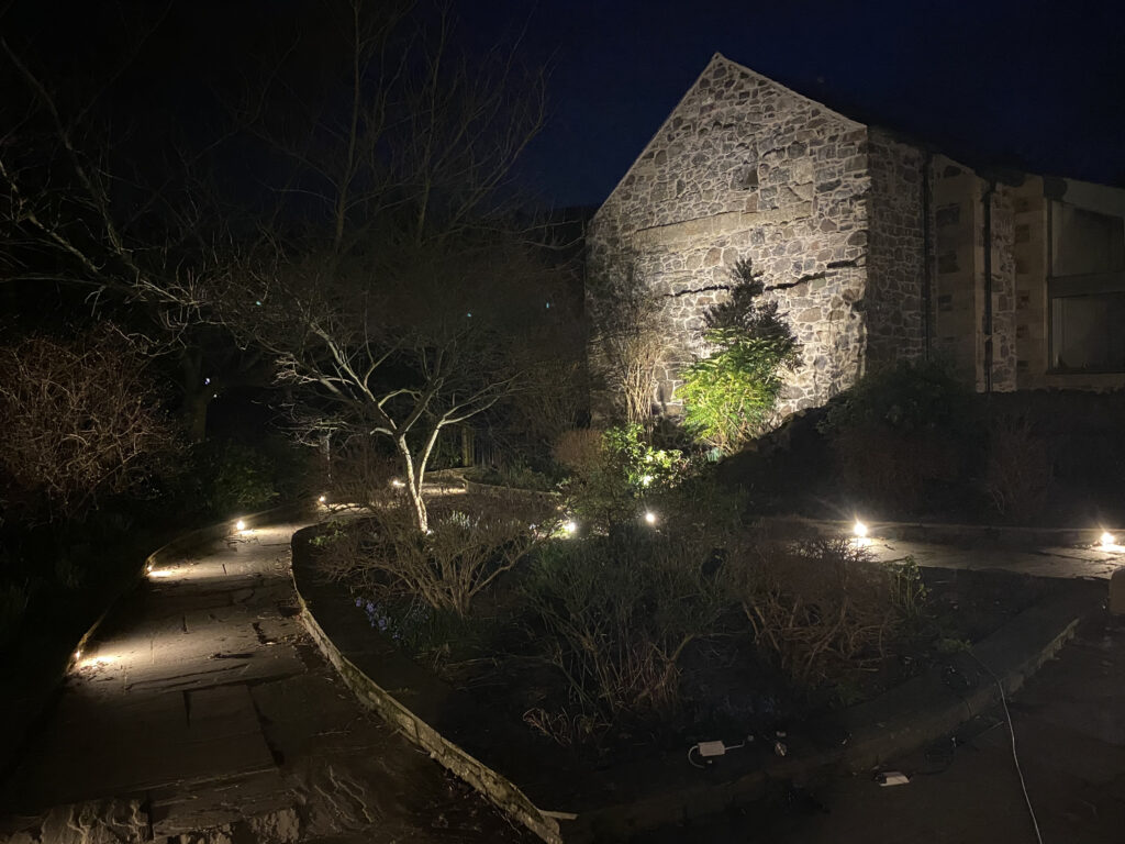 Ideas for garden lighting. A photo of a stone house exterior and garden path illuminated at night
