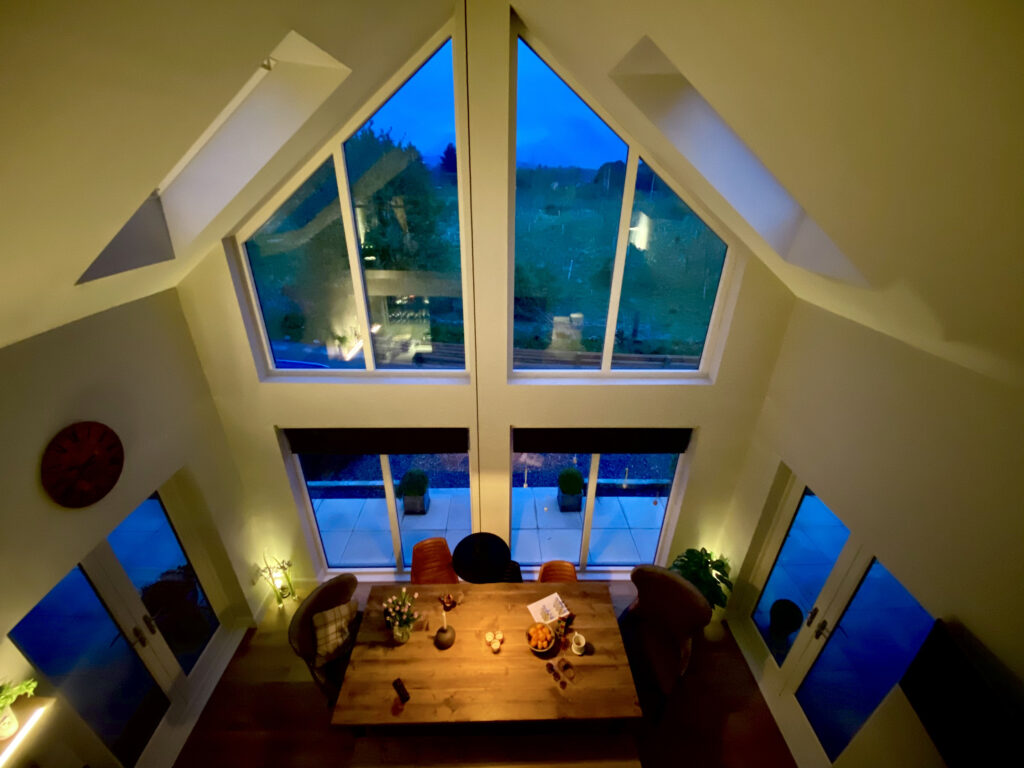 Top tips for cosy lighting in your home. A high angle photo of a modern dining room interior with large window illuminated at dusk